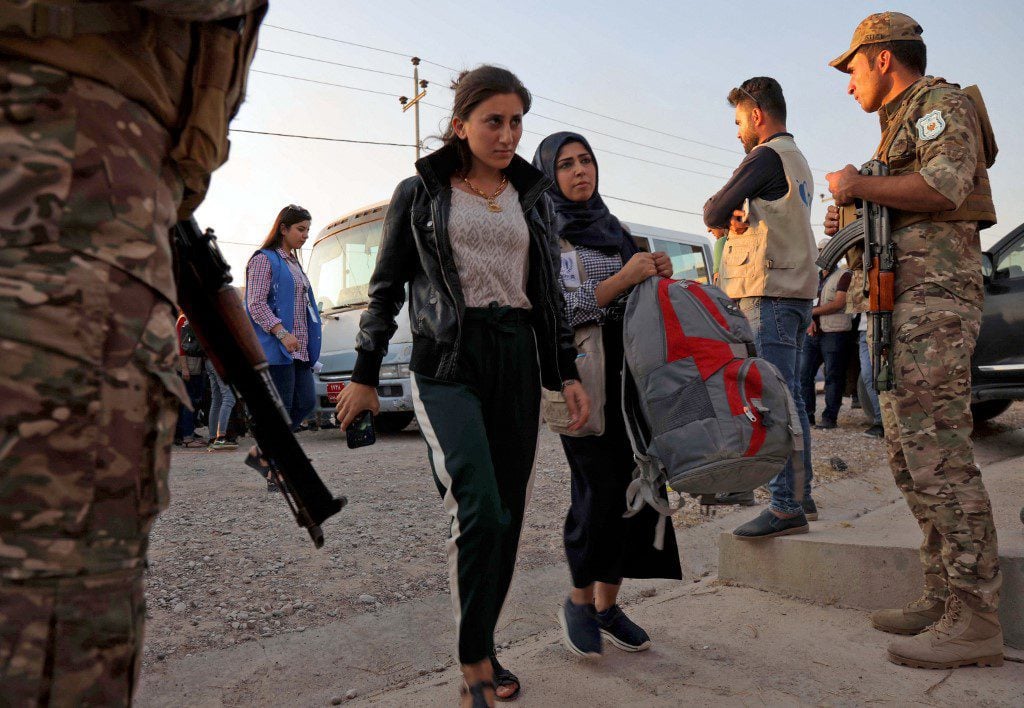 Two women walk after disembarking from a minibus transporting Syrians fleeing the ongoing Turkish military operation in northeastern Syria