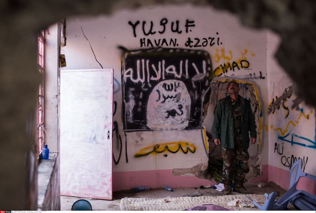 A Kurdish Peshmerga fighter gives a tour of Islamic State hideouts in the newly liberated city of Sinjar. Yazidi members of the Kurdish forces have already covered over some of the graffiti with their own. January 2016, Sinjar, Iraq. Photo Laurence Geia/SIPA. 